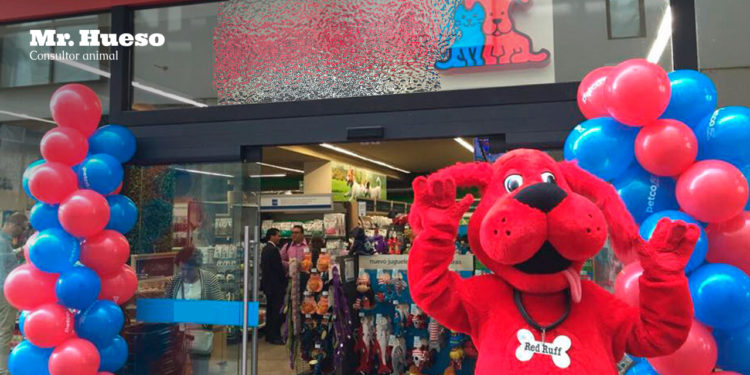 Aparece una persona disfrazada de perro, de color rojo, en la puerta de una tienda de animales llena de globos azules y rojos
