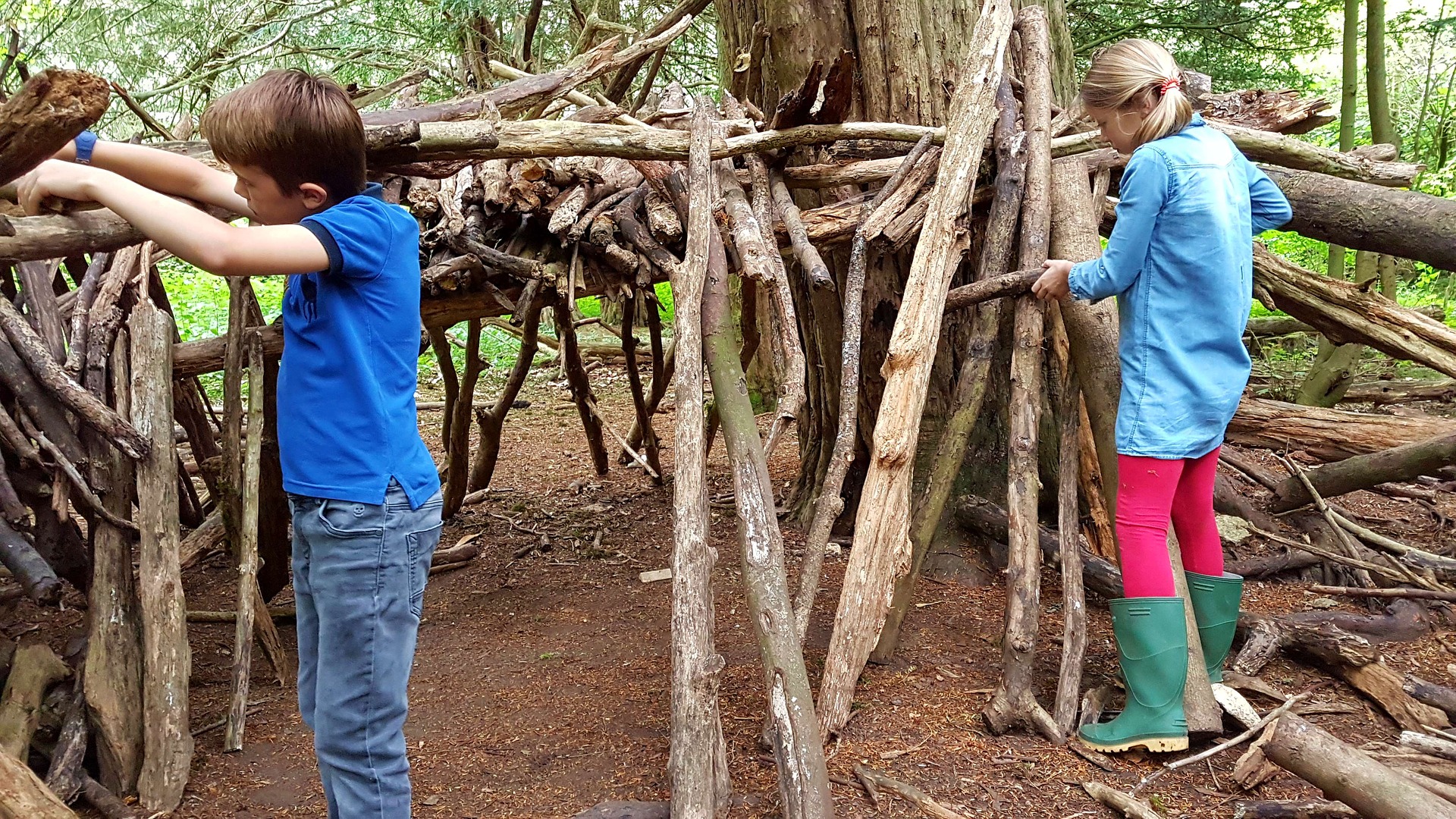 niño y niña haciendo una cabaña con troncos secos