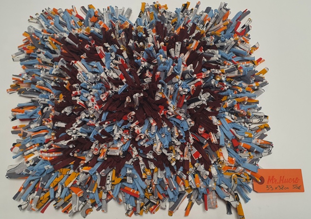 alfombra olfativa de tonos azul, granate, gris y amarillo de 33 por 38 centímetros y etiqueta naranja